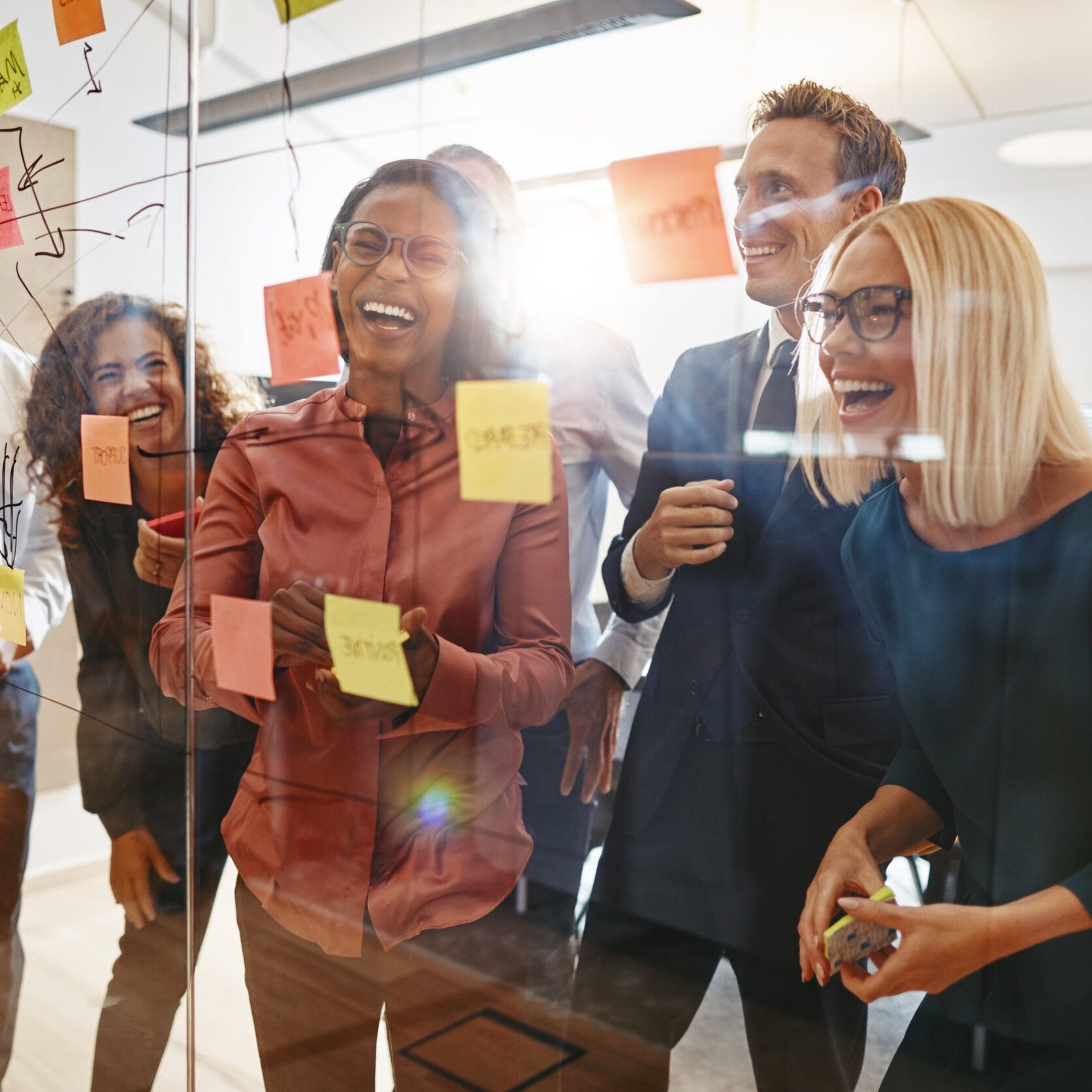 Laughing group of diverse businesspeople having a brainstorming session together with sticky notes in an office